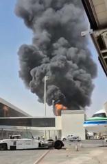 Smoke rises beside an airport terminal as an airliner stands at a gate