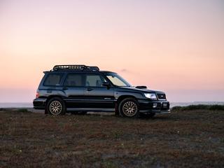A first-generation Subaru Forester bearing STi badges, by the sea at dusk